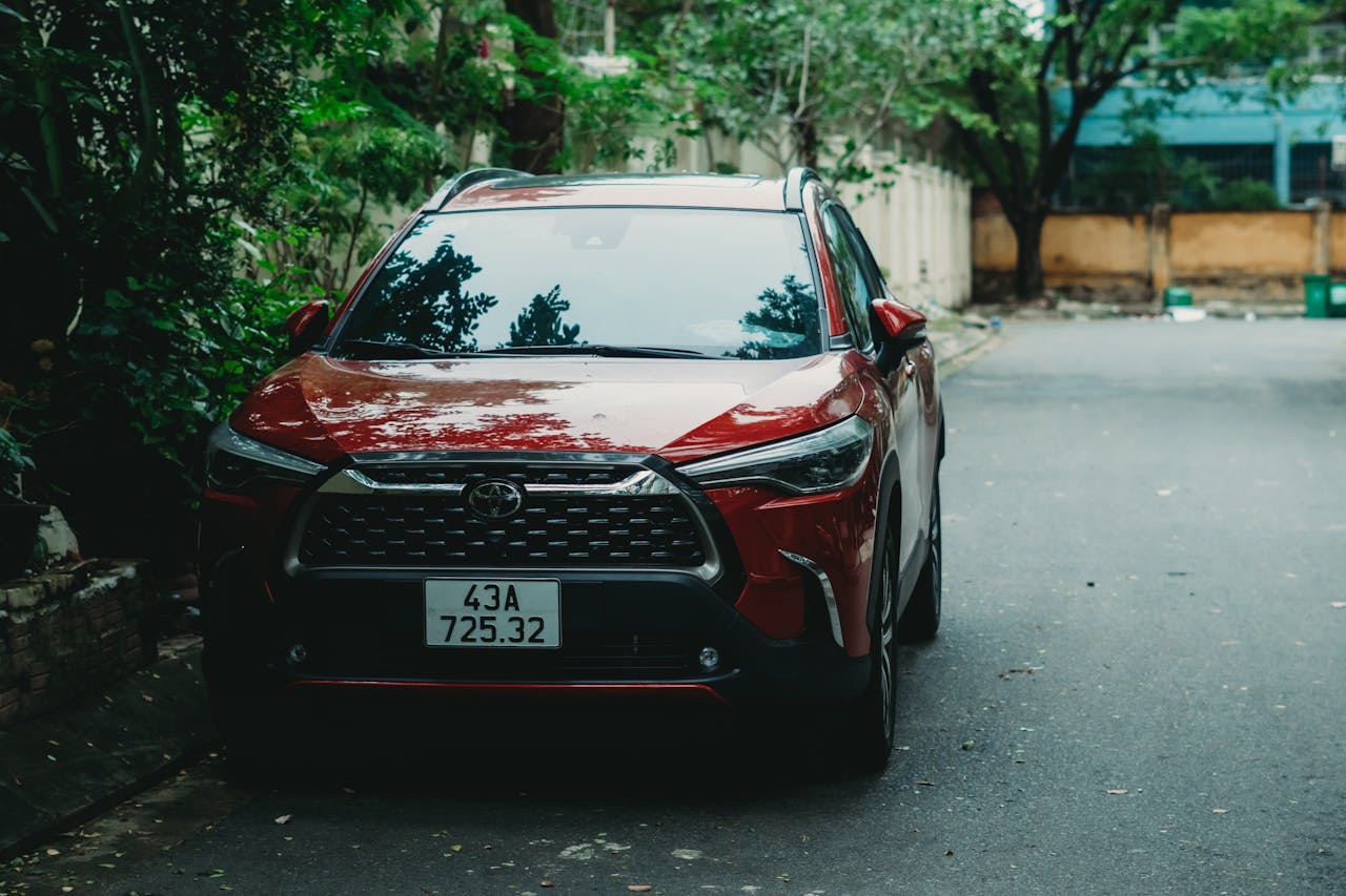 A red Toyota Corolla Cross parked outdoors on a quiet street with greenery.